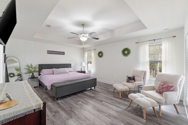 bedroom with baseboards, a tray ceiling, visible vents, and wood finished floors