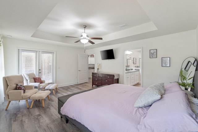 bedroom with a tray ceiling, access to outside, connected bathroom, light wood finished floors, and visible vents