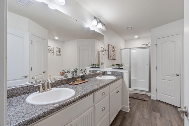 full bath featuring visible vents, a sink, a shower stall, and wood finished floors