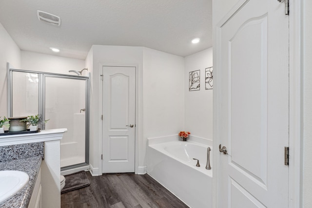 full bath with a shower stall, wood finished floors, a textured ceiling, a bath, and visible vents