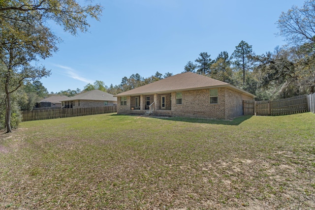 back of property with a fenced backyard, a lawn, and brick siding
