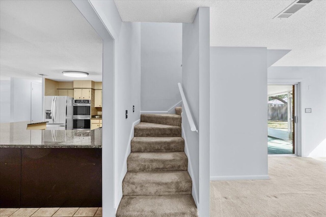 stairs with carpet, baseboards, a textured ceiling, and visible vents