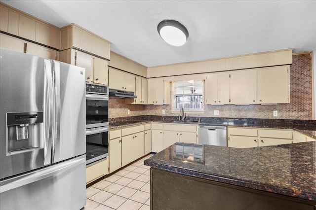 kitchen with decorative backsplash, cream cabinetry, appliances with stainless steel finishes, under cabinet range hood, and a sink
