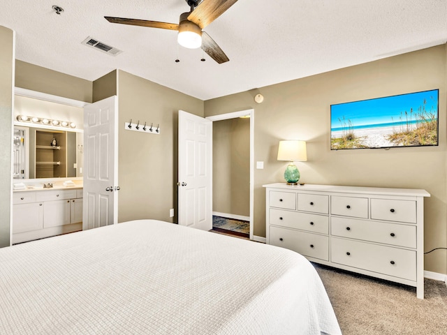 bedroom with ensuite bathroom, carpet, a textured ceiling, visible vents, and baseboards