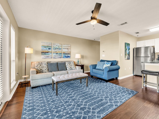living room with dark wood-type flooring, visible vents, ceiling fan, and baseboards