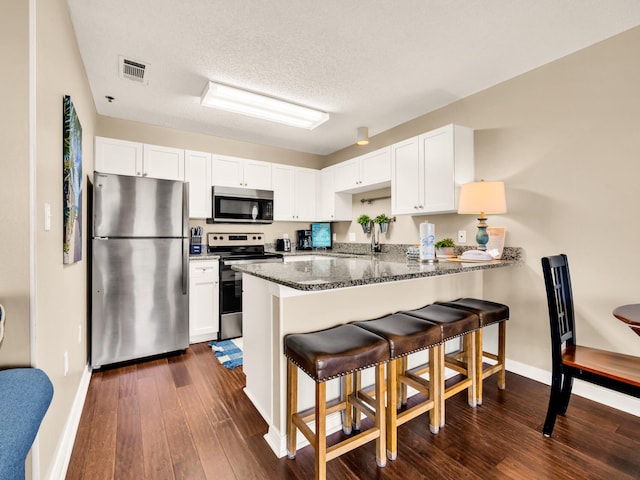 kitchen featuring white cabinets, a kitchen bar, a peninsula, and stainless steel appliances
