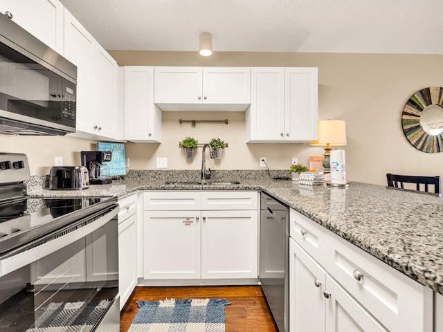 kitchen featuring a sink, appliances with stainless steel finishes, white cabinetry, wood finished floors, and light stone countertops