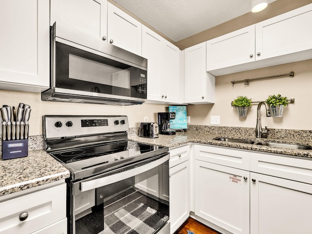 kitchen featuring a textured ceiling, white cabinets, light stone counters, a sink, and stainless steel appliances