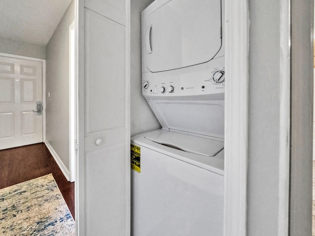 clothes washing area featuring laundry area, stacked washer and dryer, dark wood-style flooring, and baseboards