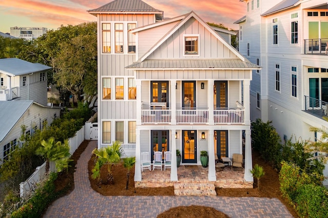back of property at dusk featuring a balcony, fence, a standing seam roof, and board and batten siding