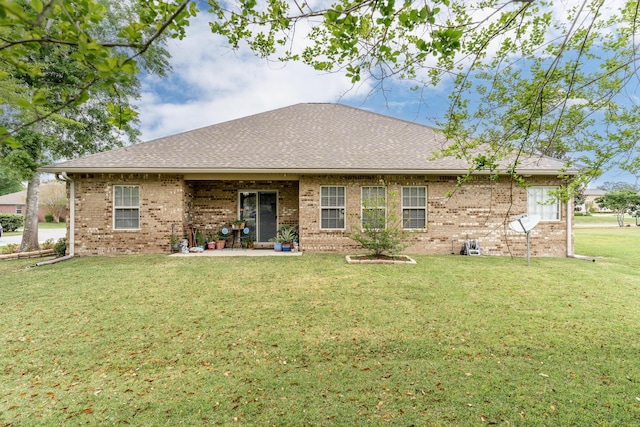 back of property with a patio area, roof with shingles, brick siding, and a yard