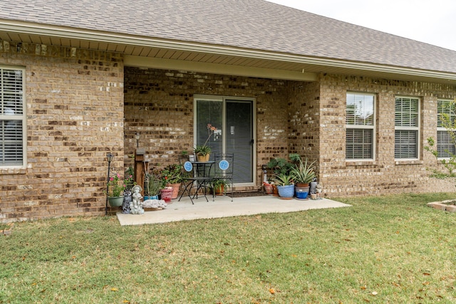 doorway to property featuring brick siding, a lawn, and a shingled roof