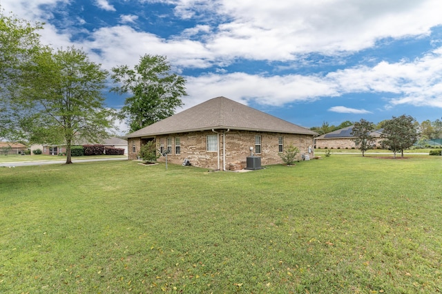 view of side of property with a lawn, brick siding, roof with shingles, and cooling unit