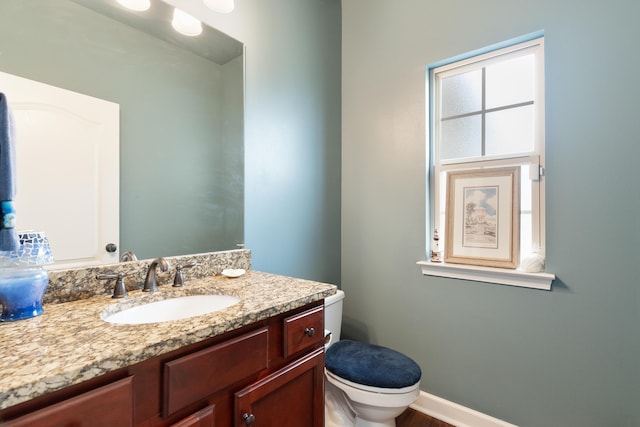 half bathroom with baseboards, vanity, and toilet