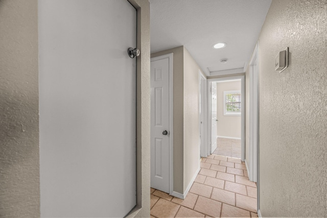 hall featuring a textured wall and light tile patterned floors