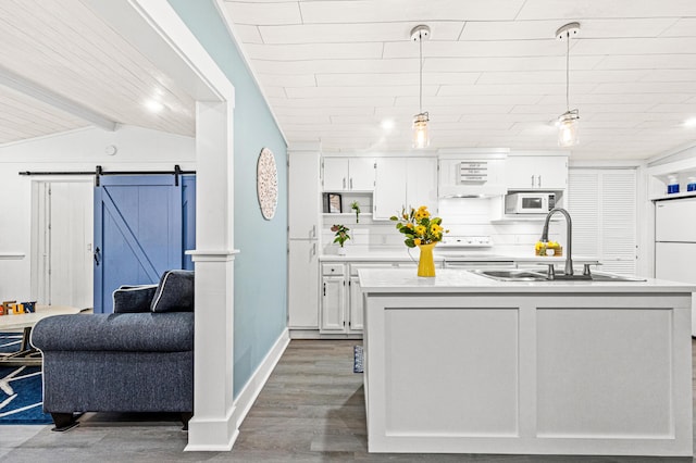 kitchen with a barn door, wood finished floors, a sink, white appliances, and white cabinets