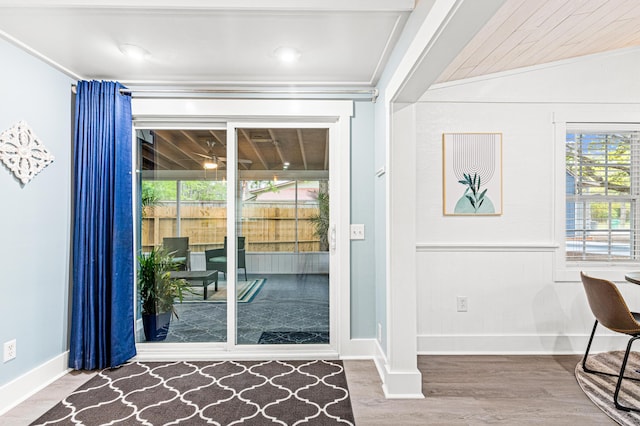 doorway to outside with lofted ceiling, crown molding, wood finished floors, and baseboards