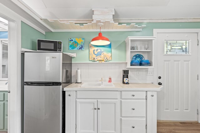 kitchen with a sink, white cabinetry, light countertops, wainscoting, and freestanding refrigerator
