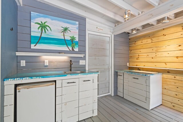 kitchen with fridge, beam ceiling, wooden walls, light wood-style flooring, and white cabinets