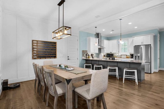 dining room featuring a decorative wall, wood finished floors, a chandelier, crown molding, and recessed lighting