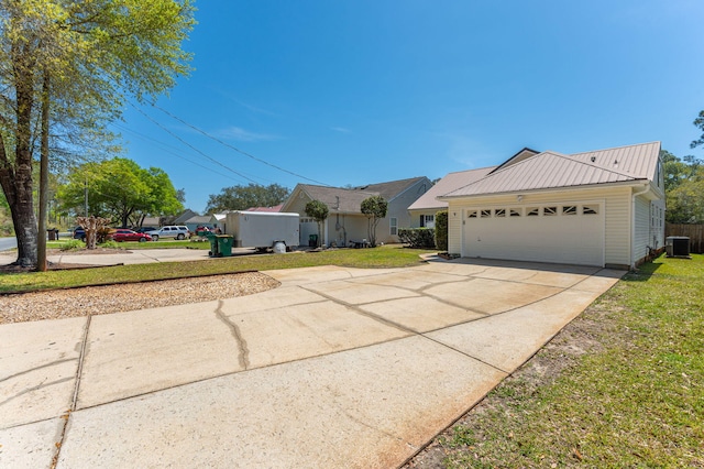 view of side of home with concrete driveway, metal roof, central AC unit, a garage, and a yard