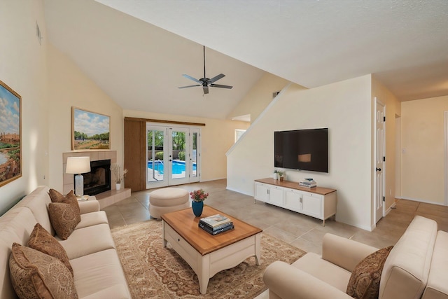 living room featuring lofted ceiling, french doors, light tile patterned flooring, ceiling fan, and a tiled fireplace
