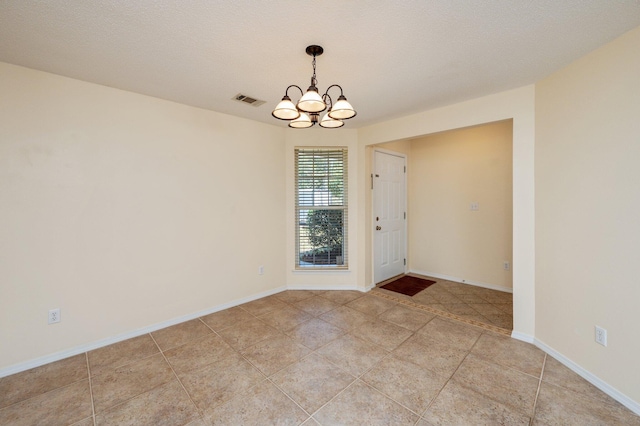 spare room with a notable chandelier, a textured ceiling, light tile patterned floors, baseboards, and visible vents