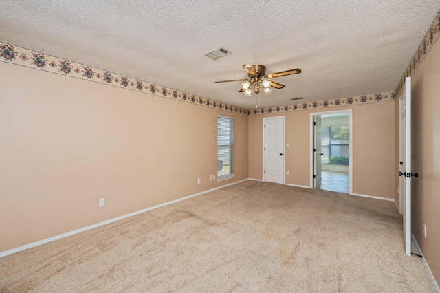 empty room with carpet, baseboards, a textured ceiling, ceiling fan, and visible vents