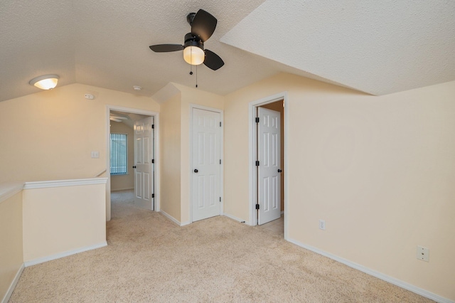 unfurnished room featuring lofted ceiling, carpet, baseboards, a textured ceiling, and a ceiling fan