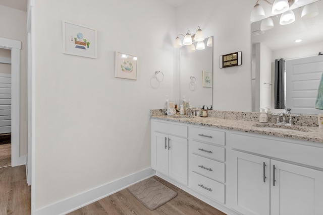 bathroom with baseboards, wood finished floors, a sink, and double vanity