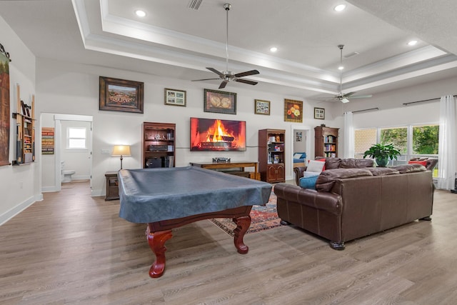 game room with a tray ceiling, crown molding, light wood-style floors, and a ceiling fan