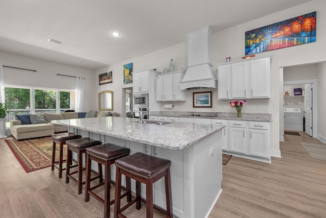 kitchen with custom exhaust hood, a sink, light wood finished floors, white cabinetry, and appliances with stainless steel finishes