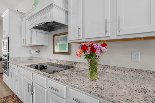 kitchen with black electric cooktop, stainless steel oven, white cabinetry, and custom range hood