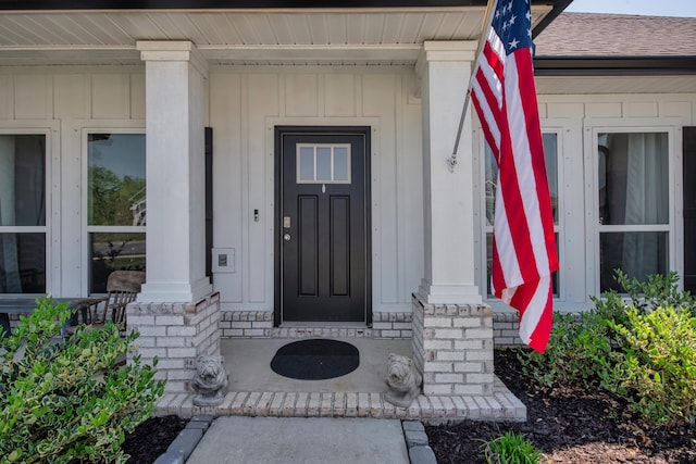 property entrance featuring roof with shingles, board and batten siding, and covered porch