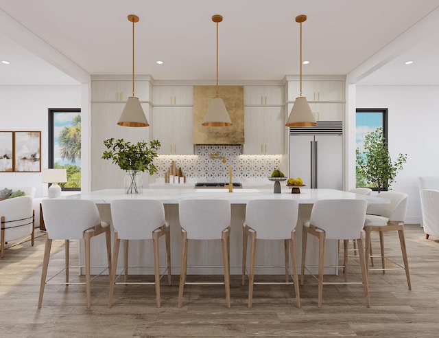 kitchen with light countertops, built in refrigerator, decorative backsplash, an island with sink, and modern cabinets
