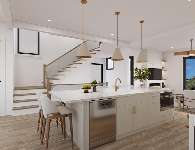 kitchen with a sink, appliances with stainless steel finishes, an island with sink, and light wood-type flooring