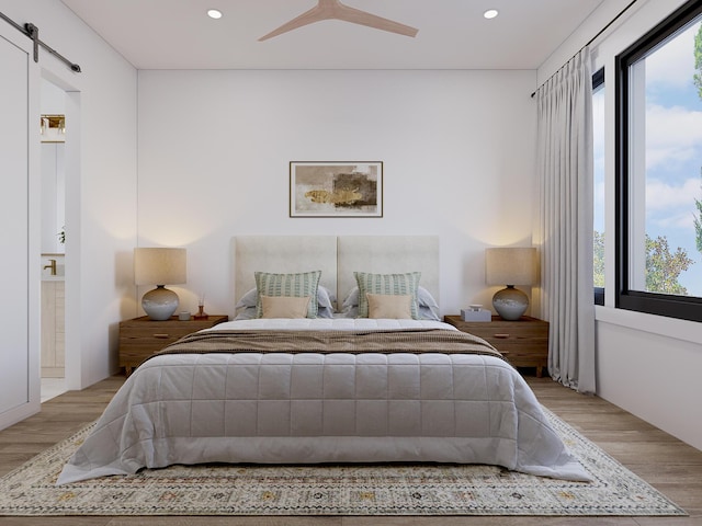 bedroom featuring ensuite bathroom, a barn door, light wood-style flooring, and recessed lighting