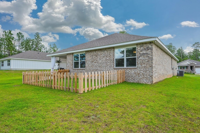 rear view of house with central air condition unit, a yard, and brick siding