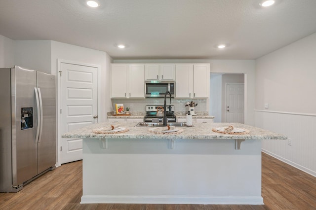 kitchen with a sink, stainless steel appliances, white cabinetry, and wood finished floors