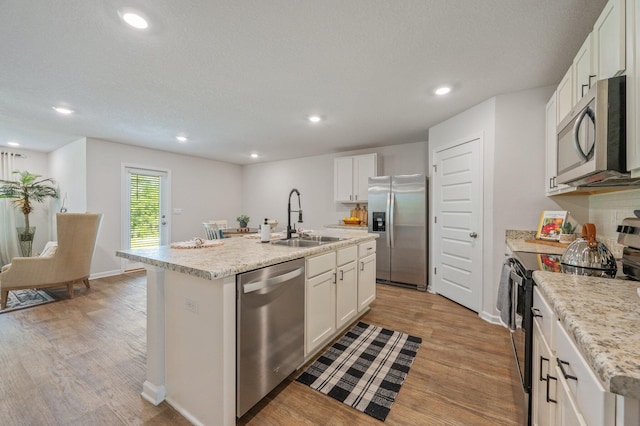 kitchen with a center island with sink, recessed lighting, a sink, light wood-style flooring, and stainless steel appliances