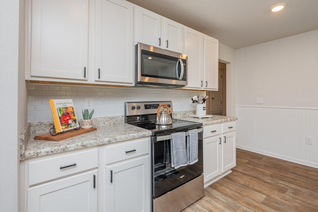 kitchen with wainscoting, light wood-style floors, white cabinetry, tasteful backsplash, and stainless steel appliances