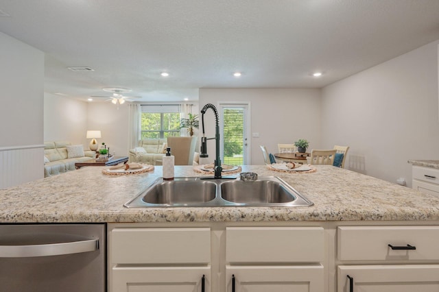kitchen featuring a ceiling fan, stainless steel dishwasher, a sink, white cabinets, and open floor plan