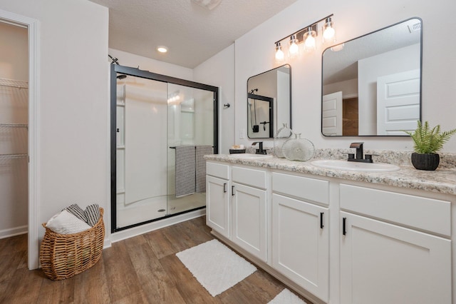 bathroom featuring double vanity, wood finished floors, a spacious closet, a shower stall, and a sink