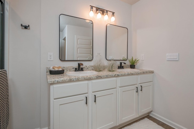 full bathroom with double vanity, baseboards, a sink, and wood finished floors