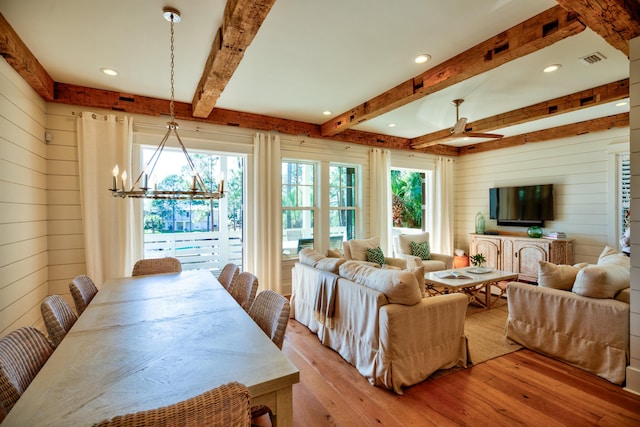 living area with visible vents, ceiling fan with notable chandelier, wooden walls, light wood-style floors, and beam ceiling