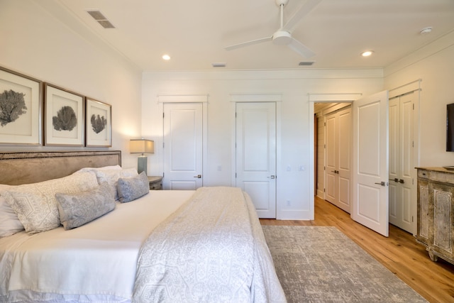 bedroom featuring ornamental molding, multiple closets, recessed lighting, visible vents, and light wood-style flooring