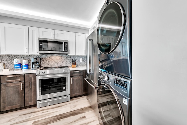 kitchen with white cabinets, light countertops, stacked washer / drying machine, stainless steel appliances, and backsplash