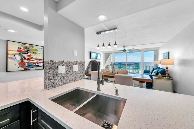 kitchen with backsplash, a sink, a ceiling fan, light stone countertops, and dark cabinetry