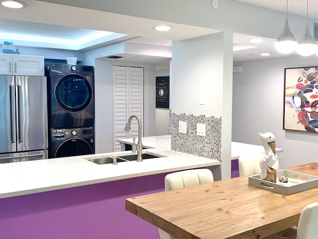 kitchen with high end fridge, decorative backsplash, hanging light fixtures, a sink, and stacked washer and dryer