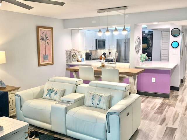 living area featuring stacked washer / drying machine, light wood-style flooring, and a ceiling fan